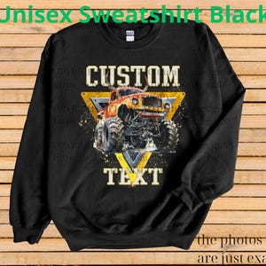 May include: Black unisex sweatshirt with a graphic of a monster truck inside a yellow triangle. The words "CUSTOM" and "TEXT" are above and below the truck. The sweatshirt has long sleeves and a crew neck.