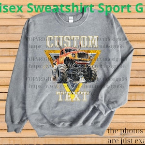 May include: A gray unisex sweatshirt with a graphic of a monster truck inside a yellow triangle. The text "CUSTOM TEXT" is displayed on the design. The words "Unisex Sweatshirt Sport Grey" are at the top.