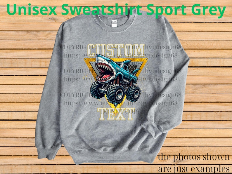 May include: A gray unisex sweatshirt with a shark monster truck graphic. The shark truck is blue and white with large black tires, set against a yellow triangle. The text "CUSTOM TEXT" is above and below the graphic. The words "Unisex Sweatshirt Sport Grey" are at the top.