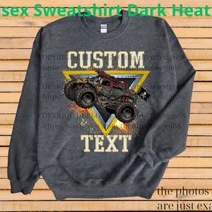 May include: Dark heather gray unisex sweatshirt with a custom design. The design features a monster truck graphic inside a yellow triangle, with the words "CUSTOM TEXT". The sweatshirt is a comfortable, casual style.