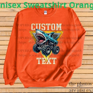 May include: Orange unisex sweatshirt featuring a graphic of a shark-themed monster truck with the words "CUSTOM TEXT". The design is in blue, white, and yellow. The sweatshirt has a crew neck and long sleeves.