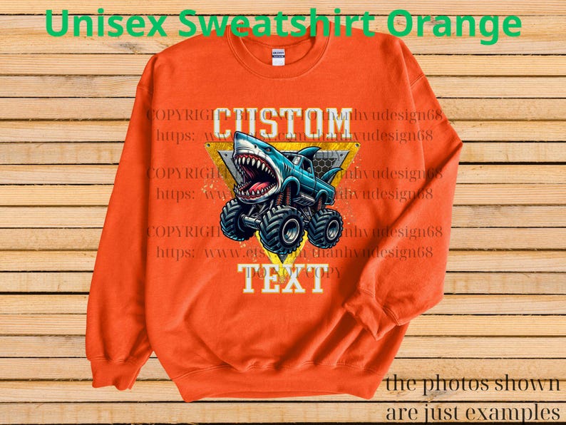 May include: Orange unisex sweatshirt featuring a graphic of a shark-themed monster truck with the words "CUSTOM TEXT". The design is in blue, white, and yellow. The sweatshirt has a crew neck and long sleeves.