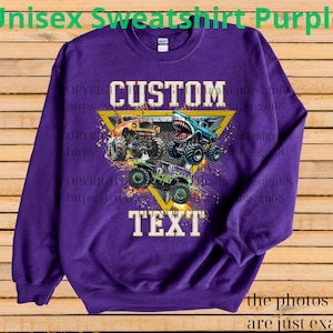 May include: Purple unisex sweatshirt with a graphic of three monster trucks. The design includes the words "CUSTOM" and "TEXT" in a yellow triangle. The text "Unisex Sweatshirt Purple" is at the top.