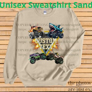 May include: Sand-colored unisex sweatshirt featuring a graphic of monster trucks, including a shark-themed truck. The design includes the text "CUSTOM TEXT" and "Unisex Sweatshirt Sand". The photos shown are just examples.