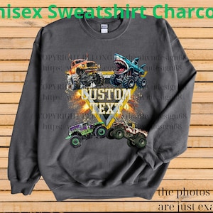 May include: Charcoal gray unisex sweatshirt featuring a graphic of four monster trucks with the text "CUSTOM TEXT" in a yellow and white design. The sweatshirt has the text "Unisex Sweatshirt Charcoal" at the top and "the photos shown are just examples" at the bottom.
