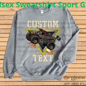 May include: A gray unisex sweatshirt with a custom design featuring a monster truck graphic. The design includes the word "CUSTOM" above the truck and "TEXT" below it, set within a yellow triangle. The sweatshirt has the text "Unisex Sweatshirt Sport Grey".