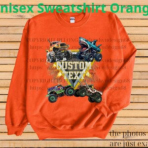 May include: Orange unisex sweatshirt featuring a graphic of monster trucks with the text "CUSTOM TEXT". The sweatshirt has long sleeves and a crew neck. The text "Unisex Sweatshirt Orange" is at the top of the image.