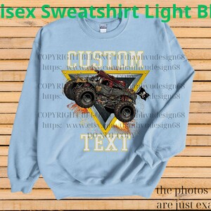 May include: Light blue unisex sweatshirt with a monster truck graphic. The design includes a red and black monster truck with a skull and crossbones flag, set against a yellow triangle. The text "CUSTOM TEXT" is also visible.