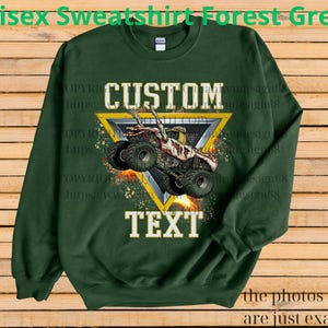 May include: Forest green unisex sweatshirt featuring a monster truck graphic within a yellow triangle. The words "CUSTOM" and "TEXT" are printed above and below the truck image. The text "the photos shown are just examples" is at the bottom.