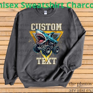 May include: Charcoal gray unisex sweatshirt featuring a shark-themed monster truck design. The graphic includes the words "CUSTOM TEXT" in a yellow triangle. The sweatshirt is a long-sleeved crew neck.