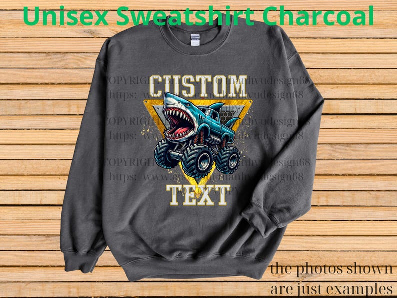 May include: Charcoal gray unisex sweatshirt featuring a shark-themed monster truck design. The graphic includes the words "CUSTOM TEXT" in a yellow triangle. The sweatshirt is a long-sleeved crew neck.