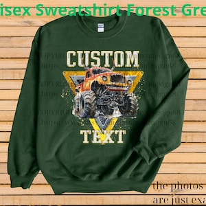 May include: Forest green unisex sweatshirt with a graphic of a monster truck inside a yellow triangle. The text "CUSTOM TEXT" is above and below the truck. The words "Unisex Sweatshirt Forest Green" are at the top.