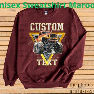 May include: Maroon unisex sweatshirt featuring a custom design of an orange monster truck inside a yellow triangle. The text "CUSTOM" and "TEXT" are displayed above and below the truck. The phrase "the photos shown are just examples" is at the bottom.