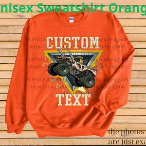 May include: Orange unisex sweatshirt featuring a monster truck design. The graphic includes a monster truck within a yellow and black triangle, with the words "CUSTOM TEXT" in white. The sweatshirt has a crew neck and long sleeves.
