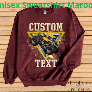 K&ouml;nnte beinhalten: Burgunderfarbenes Unisex-Sweatshirt mit einem gelb-schwarzen Monster-Truck-Design in einem gelben Dreieck. Die W&ouml;rter "CUSTOM" und "TEXT" befinden sich &uuml;ber und unter der Truck-Grafik. Der Text "Unisex Sweatshirt Maroon" steht oben.