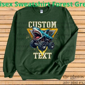 May include: Forest green unisex sweatshirt with a graphic of a shark-themed monster truck. The design includes the words "CUSTOM" and "TEXT" in a yellow triangle. The text "Unisex Sweatshirt Forest Green" is at the top.