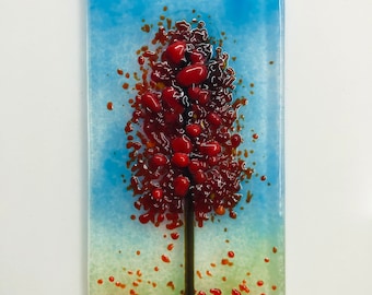 May include: A glass art piece depicting a red tree with a brown trunk against a blue and green background.