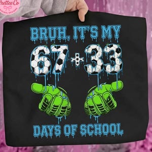 Może przedstawiać: Czarna koszulka z napisem "BRUH, IT'S MY 67 + 33 DAYS OF SCHOOL" w kolorze niebieskim. Cyfry zaprojektowano jako piłki nożne z niebieskimi, ociekającymi akcentami. Zielone rękawice bramkarskie na dole.