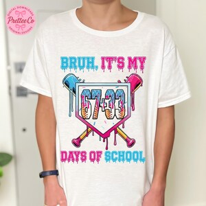 Pode incluir: Camiseta branca com um design gr&aacute;fico colorido. O design apresenta o texto "BRUH, IT'S MY" acima de um gr&aacute;fico tem&aacute;tico de beisebol com os n&uacute;meros "67-33" e as palavras "DAYS OF SCHOOL". O design inclui tacos de beisebol e efeitos de tinta pingando.