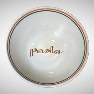 May include: A white ceramic bowl featuring a circular rim decorated with thin red and green stripes. The interior center of the bowl displays the word pasta written in a stylized font with alternating red and green vertical lines on the letters.