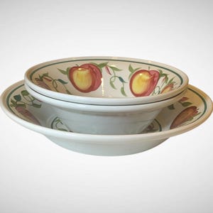 May include: Two white ceramic bowls, one stacked inside the other, with a matching plate. The bowls and plate feature a painted design of peaches and green leaves with a green border. The bowls are ideal for serving soup or salad.