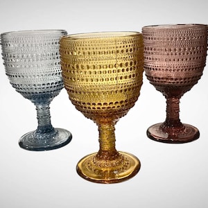 May include: Three decorative wine glasses in shades of blue, gold, and rose. Each glass features a textured, dotted pattern on the bowl and stem. The glasses are designed for serving wine or other beverages.
