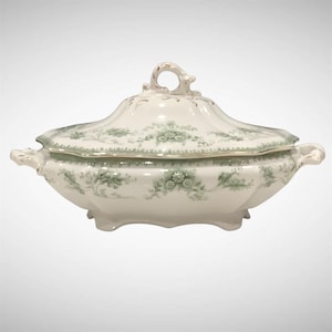 May include: A white porcelain serving dish with a lid, featuring a delicate green floral pattern. The dish has a scalloped edge, gold trim, and a loop handle on the lid. It has two side handles and rests on small feet.