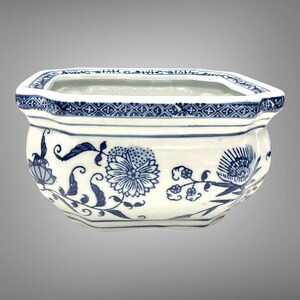 May include: A white ceramic planter with a hexagonal shape, featuring blue floral patterns and a geometric border along the top rim. The vessel has a smooth, glossy finish and a wide opening, showcasing detailed botanical illustrations in blue ink.