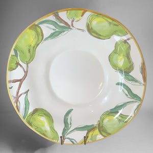 May include: White ceramic serving bowl with a pear design. The bowl features a wide rim with a gold edge and a central well. Green pears and leaves are painted around the rim, creating a decorative border.