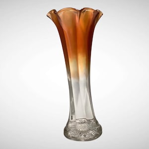 May include: A tall, elegant glass vase with a flared, ruffled rim. The vase transitions from a warm orange hue at the top to clear glass at the base. The base features a decorative, etched floral pattern. A decorative piece for the home.