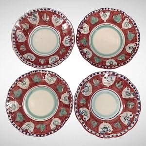 May include: A set of four round ceramic plates with scalloped edges. Each plate features a central cream-colored circle surrounded by a wide terracotta-red border decorated with repeating white bird illustrations and green leaf accents.