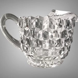 May include: Clear glass creamer with a geometric cube pattern. The creamer has a handle and a spout for easy pouring. The design is a classic style, perfect for serving cream or milk.