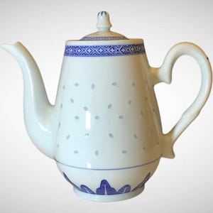 May include: White porcelain teapot with a curved spout and handle. The teapot features a blue geometric pattern around the rim and base, with a series of small, leaf-shaped cutouts. The lid is topped with a small finial.