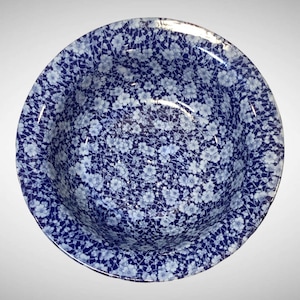 May include: A round ceramic bowl featuring a dense, all-over pattern of small, light blue flowers set against a deep navy blue background. The interior and rim of the bowl are fully covered in this intricate floral design, creating a uniform look.
