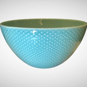 May include: A turquoise ceramic bowl with a glossy finish. The exterior features a pattern of small, evenly spaced white dots. The interior of the bowl is a muted green color. This decorative bowl is suitable for serving or display.