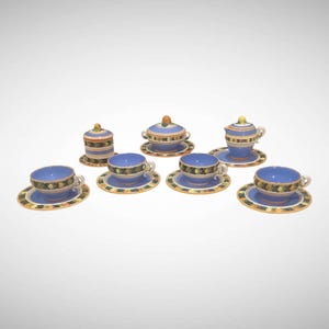 May include: A ceramic tea set featuring a light blue glaze with a decorative band of green, yellow, and black floral patterns. The set includes four teacups with saucers, a lidded sugar bowl, and a lidded creamer, all with matching motifs.