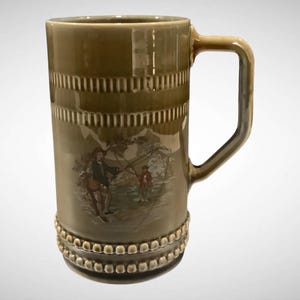 May include: A tall, olive-green ceramic beer stein with a handle. The stein features a detailed illustration of figures in a landscape. Decorative horizontal bands and a beaded base add to the stein's design. A classic piece for beer enthusiasts.