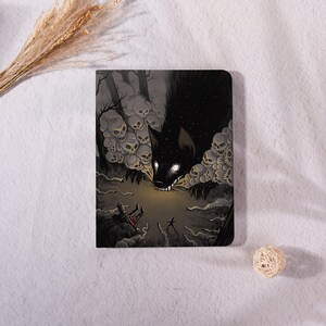 May include: A dark, rectangular notebook featuring a fantasy illustration. A large, black wolf-like creature with glowing eyes and sharp teeth is surrounded by skulls. A small figure runs from the creature in a misty, forest-like setting.