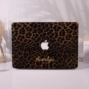 May include: A rectangular laptop cover featuring a brown and black leopard print pattern. The cover displays a centred white Apple logo and the name Averlyn written in a gold cursive script font positioned below the logo on the surface.