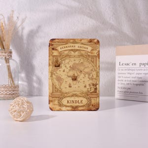 May include: A rectangular Kindle cover with a vintage world map design. The cover is tan with the words "RENAISSAN EDITION" at the top and "KINDLE" at the bottom. The map features ships and cherubs.