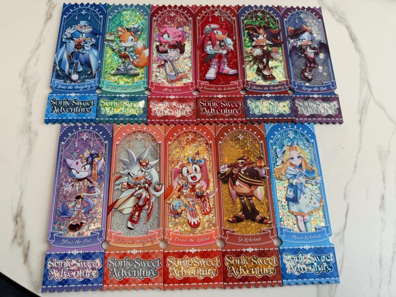 May include: Eleven rectangular bookmarks featuring Sonic the Hedgehog characters in ornate outfits with glittery backgrounds. Each bookmark displays a character name and the text Sonic Sweet Adventure in a decorative script at the bottom edge.