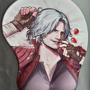 May include: Ergonomic mousepad featuring a stylized illustration of a character with white hair, wearing a red jacket and gray shirt. The character is holding a strawberry. The mousepad has a wrist rest and a white background.