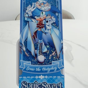 May include: A rectangular blue shaker bookmark featuring an illustration of Sonic the Hedgehog wearing a formal outfit with a top hat and cape. The design includes glittery blue accents, a cupcake graphic, and the text Sonic the Hedgehog and Sonic Sweet Adventure printed in a decorative font.