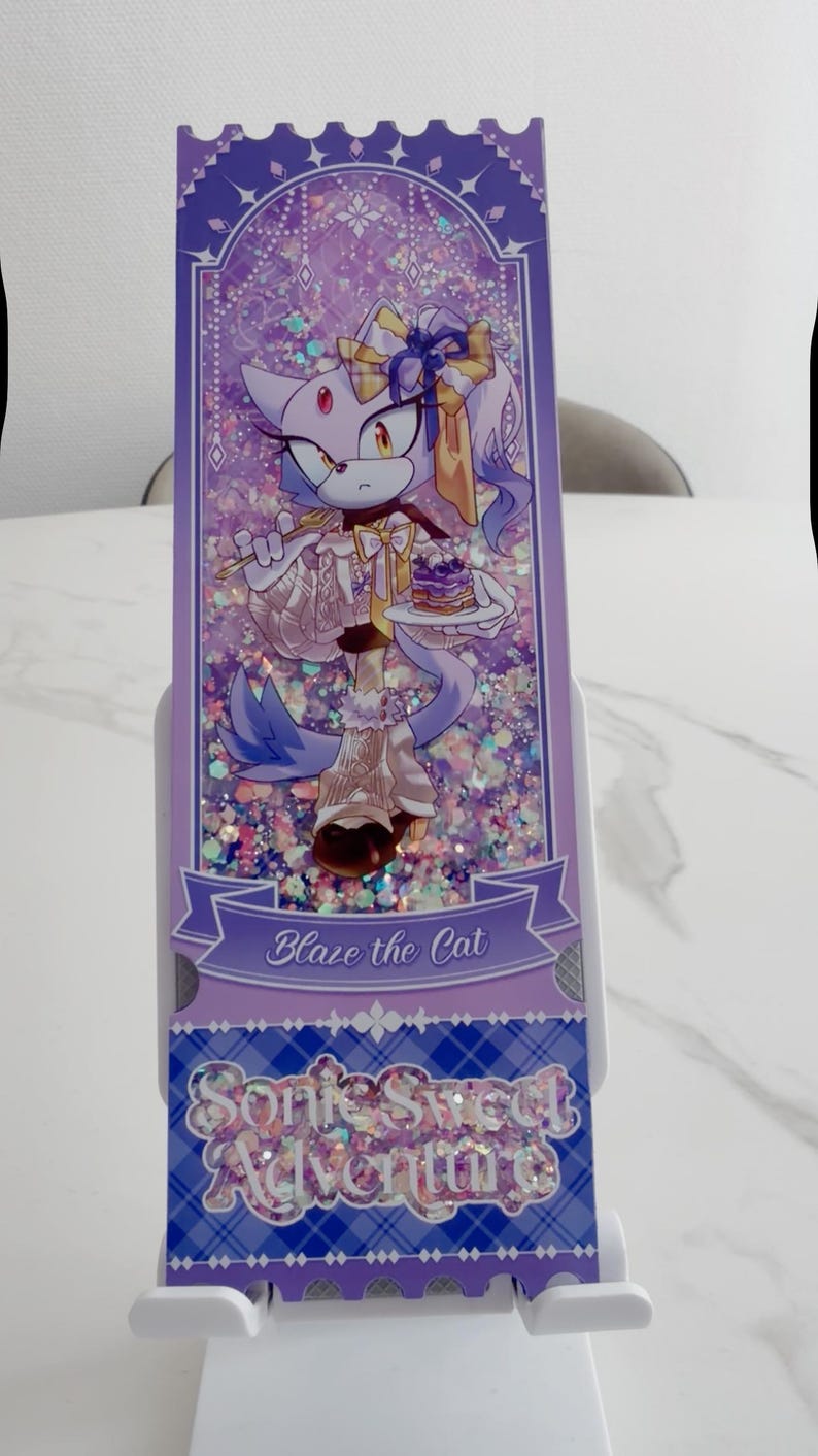 May include: A rectangular purple shaker bookmark featuring an illustration of Blaze the Cat holding a small cake. The design includes holographic glitter, a banner with the text Blaze the Cat, and a bottom section with the text Sonic Sweet Adventure.