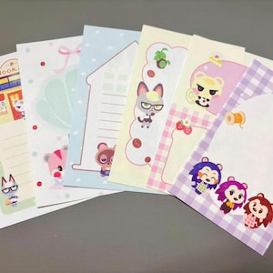 May include: A collection of colorful stationery featuring various cartoon animal characters. The designs include a house, coffee beans, and gingham patterns. The stationery is in shades of pink, blue, yellow, and purple.