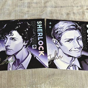 May include: Two art prints featuring portraits of Sherlock Holmes and John Watson. The Sherlock print has the name "Sherlock" in cursive and the name "Sherlock Holmes" in a vertical font. The John Watson print has the name "John" in cursive and the name "John Watson" in a vertical font.