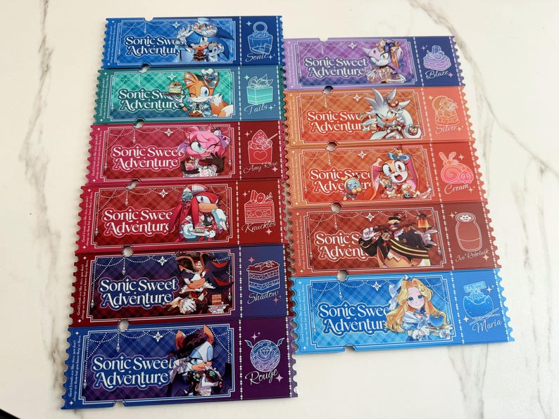 May include: A collection of twelve rectangular paper tickets featuring Sonic Sweet Adventure branding. Each ticket displays a unique character illustration, a dessert icon, and the text Sonic Sweet Adventure in a stylized white script font.