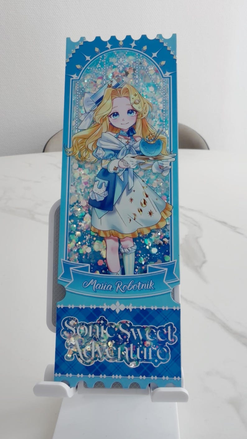 May include: A rectangular shaker bookmark featuring an anime-style illustration of Maria Robotnik in a blue and white dress holding a blue bowl. The background contains iridescent glitter. Text reads Maria Robotnik and Sonic Sweet Adventure.