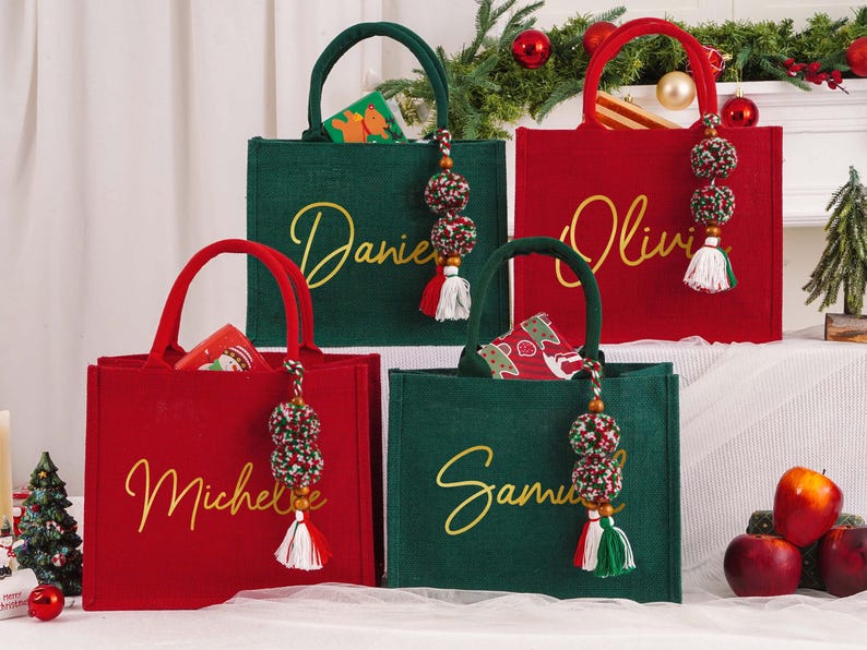 May include: Four Christmas-themed tote bags in red and green, each with a name in gold script. The bags have matching handles and decorative tassels. Some bags contain small gift boxes. Festive holiday decor is in the background.