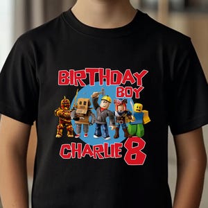 May include: A black t-shirt featuring a colorful graphic with the text "BIRTHDAY BOY CHARLIE 8" and cartoon characters. The shirt is worn by a young boy with blond hair.